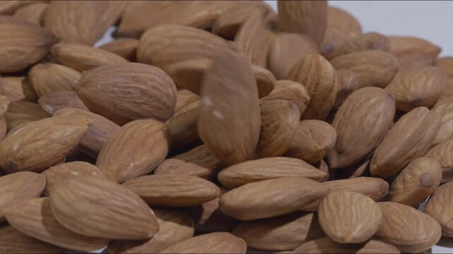Macro slow motion shot of fresh crunchy raw almonds falling and dropping onto a pile, showcasing dynamic movement, dry fruit texture, healthy snack food, and nutrition.