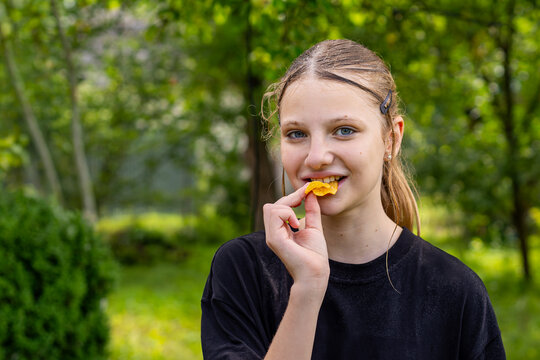 Smiling Teenage Girl Eating a Potato Chip Outdoors. Smiling teenage girl eating a potato chip in a sunlit green garden.