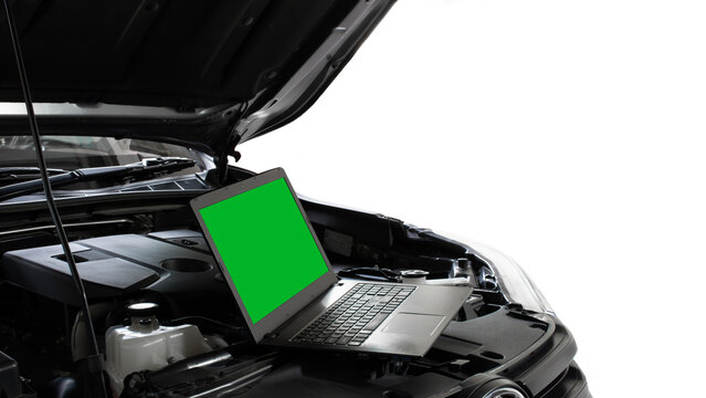 A laptop computer with a green chroma key screen sitting in an open car engine bay for modern vehicle diagnostics, software tuning, and auto repairs