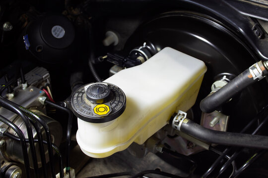 A close-up of a plastic brake fluid reservoir with a black cap mounted on a brake booster inside a clean automobile engine compartment for vehicle maintenance