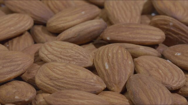 Macro rack focus transition shot shifting focus to reveal a pile of fresh raw almonds, highlighting dry fruit texture, crunchy healthy food, and organic agriculture product.