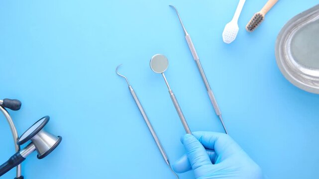 Dentist's hand in blue glove picks up dental tools from blue background with stethoscope