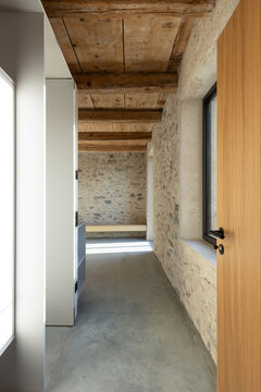 A corridor leading into an empty room with stone walls and a wooden ceiling. A beautiful renovation featuring a polished concrete floor.