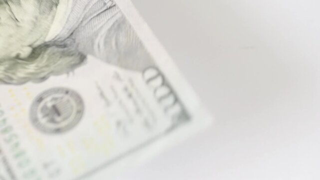 Angled edge of bill sliding across white surface, partial portrait peek, faint shadows and soft blur, minimalist composition evoking checkout, register or audit moments