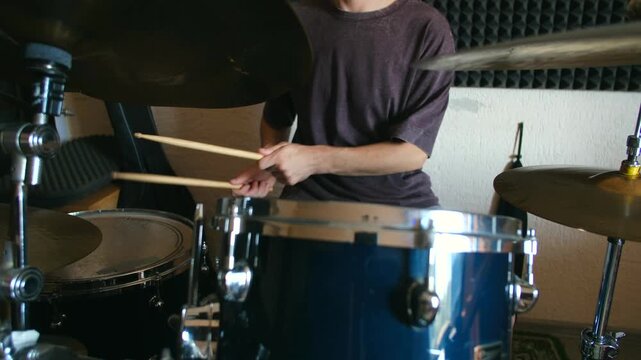 Anonymous drummer practicing beat on blue drum kit with wooden sticks in soundproofed room. Professional musician playing percussion instruments during rehearsal. Male musician playing drum kit in