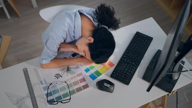 Young Hispanic woman designer falling asleep on working table in office. 