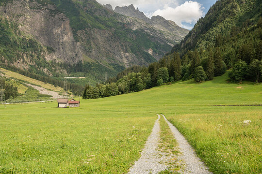 Guttannen, Switzerland. Gravel mountain trail through alpine meadow with rugged peaks in the Bernese Alps