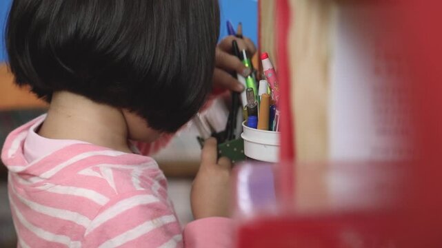 필기구가 꽂힌 통 근처에서 무언가를 정리하고 있는 아이의 뒷모습입니다.