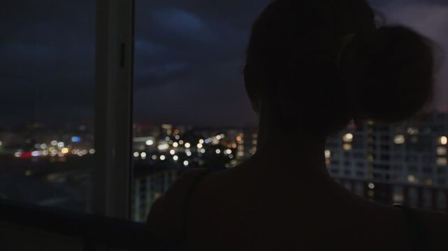 Storm over the city. Woman watches thunder storm with lightnings from the balcony of her apartment on a top floor with city view on the background