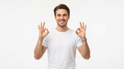 Fototapeta premium Smiling young man in a white t-shirt showing an ok gesture with both hands looking at the camera with a happy face