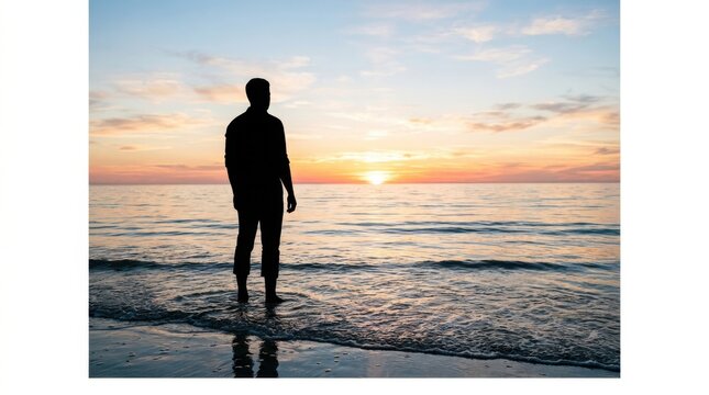 Silhouette of a man standing on the beach watching the sunset over the ocean water during a peaceful summer evening