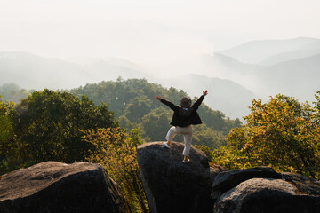 Fototapeta premium Person stands atop rugged boulders, arms wide open