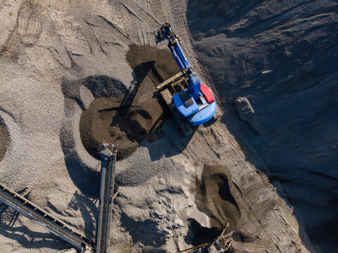 Aerial view of Blue Excavator Working Near Stone Crusher and Stockpiling Area in Industrial Mine Site, Construction and mining site view from above