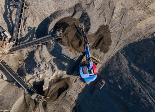 Aerial view of Blue Excavator Working Near Stone Crusher and Stockpiling Area in Industrial Mine Site, Construction and mining site view from above