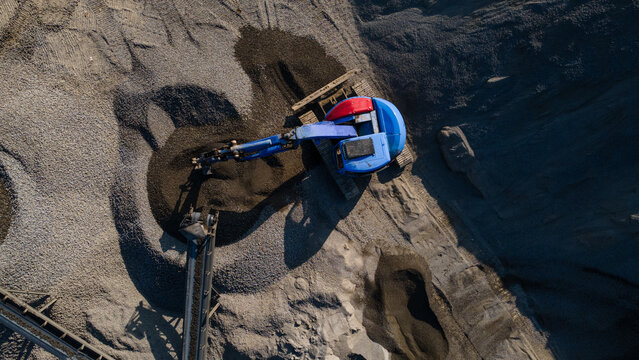 Aerial view of Blue Excavator Working Near Stone Crusher and Stockpiling Area in Industrial Mine Site, Construction and mining site view from above