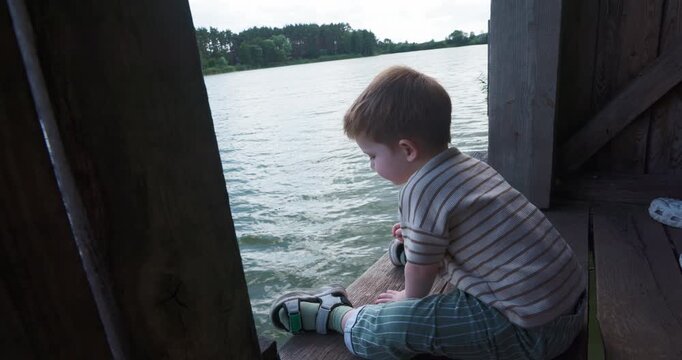 Toddler child relaxing sitting on wooden dock near river bank in summer