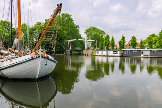 Edam, Netherlands: Traditional Dutch sailboat and wooden drawbridge with houseboats reflecting in the quiet canal of Edam.