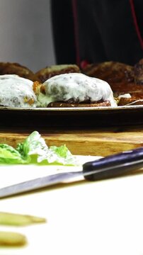 Hands of chief on commercial kitchen serves burgers on the plate - inside the restaurant