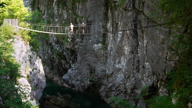 Tourists crossing a high suspension rope bridge over the deep chasm of Cellina gorge, Northern Italy