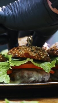 Hands of chief on commercial kitchen serves burgers on the plate - inside the restaurant