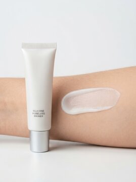A white silicone primer tube is displayed next to a smooth cosmetic cream smear on an Asian arm.