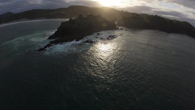 Low aerial flight along the rugged coastline of Great Barrier Island, New Zealand, revealing dramatic cliffs, ocean waves and untouched coastal landscape.