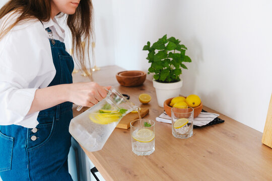 Woman pours lemonade from pitcher into glass on kitchen counter