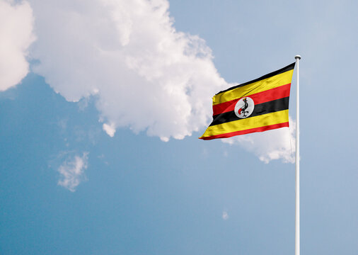Uganda national flag waving in sky with long mast.