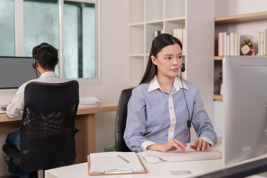 Asian call center agents with headsets working at computers in modern office