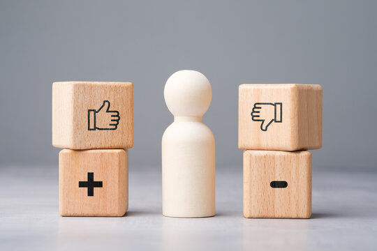 Wooden figure evaluating pros and cons between positive and negative choices for better decision making