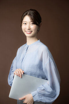 茶色背景でノートパソコンを持ってカメラ目線の日本人女性　ビジネス・キャリア・成長・目標の秋イメージ
