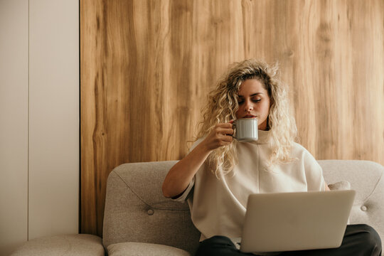 Woman working remotely on laptop drinking coffee at home