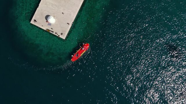 Red semi-submarine boat docking at a concrete pier with a lighthouse in Zadar, Croatia, top-down view.