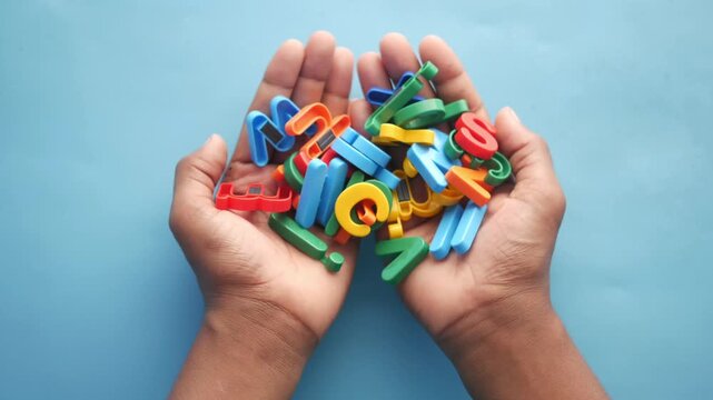 Hands holding pile of colorful plastic letters against blue background shot from top view