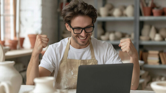 Potter's Triumph: A delighted potter, wearing an apron and glasses, celebrates enthusiastically while looking at his laptop in a studio filled with ceramic creations.