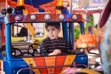 Pensive little boy driving colorful toy truck on fairground carousel © Oleksii Yemelianov