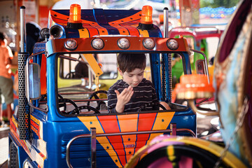 Little boy raising his hand while sitting in blue toy truck on carousel ride © Oleksii Yemelianov