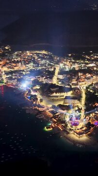 A dynamic aerial drone shot capturing the energetic nightlife of Ksamil Beach, Albania at night. The video highlights luxury beachfront clubs and open-air party venues illuminated by vibrant neon ligh
