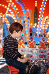 Pensive young boy sitting on elephant carousel ride with glowing lights © Oleksii Yemelianov