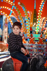 Playful little boy sticking tongue out on colorful amusement park carousel © Oleksii Yemelianov