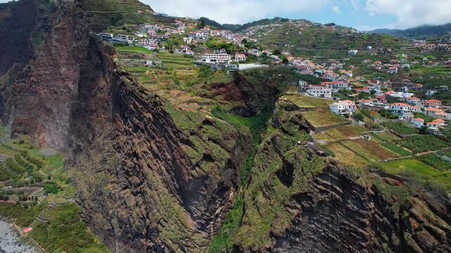 Madeira Island, dramatic vertical coastal cliffs and organic farm of Faja dos Padres- cliffside village of Quinta Grande in Camara de Lobos. Cinematic drone 4k