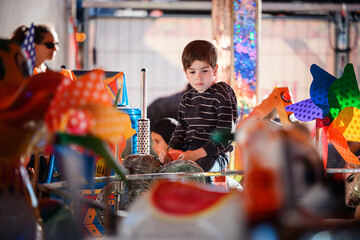 A young boy riding a carousel elephant viewed through bright colorful toy pinwheels at a funfair © Oleksii Yemelianov