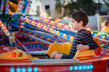Child enjoying a quiet moment on a red carousel car at an outdoor funfair © Oleksii Yemelianov