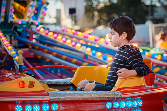 Child enjoying a quiet moment on a red carousel car at an outdoor funfair