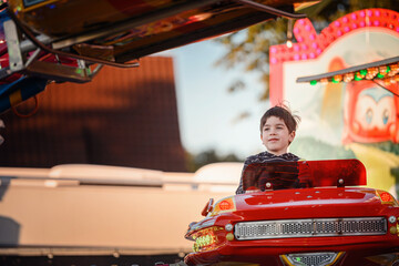 Smiling boy enjoying sunset light while sitting in red carousel ride © Oleksii Yemelianov