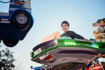 Smiling boy riding lit green carousel vehicle at outdoor amusement park © Oleksii Yemelianov