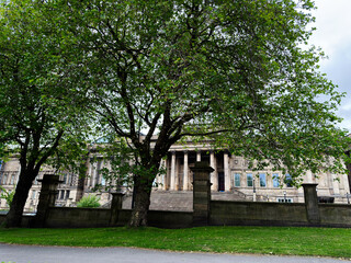 Obraz premium Historic neoclassical civic building with stone columns and grand steps framed by green trees in Liverpool, UK park