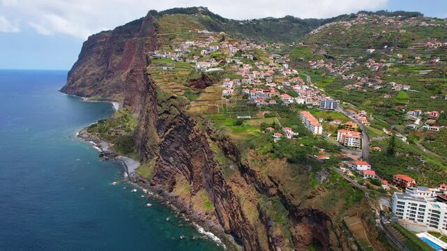 Coastal village in Camara de Lobos, Madeira - Faja dos Padres and Quinta Grande. drone backward flight along dramatic vertical cliffs, terraced green fields and 
