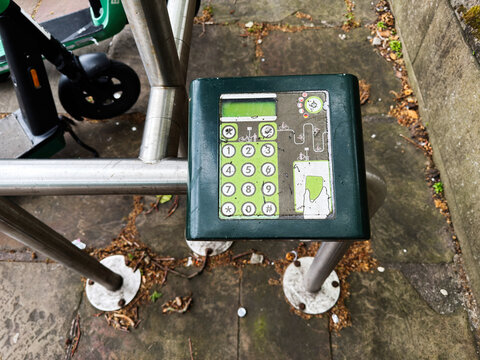 Weathered scooter and bike rental keypad payment terminal at a dock in Liverpool, UK on a stone pavement