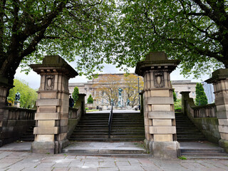 Obraz premium Grand stone St. John's Gardens entrance stairs and neoclassical museum facade framed by leafy trees, ornamental pillars and statues in Liverpool, UK